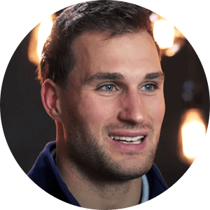 Headshot of Kirk Cousins smiling with some lights hanging overhead in the background.